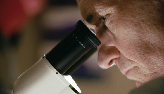 A close up photo of a man looking through a microscope